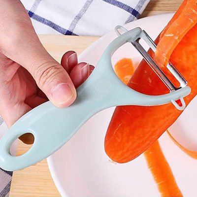 Eplucheur bleu pelant carotte au dessus d'une assiette blanche