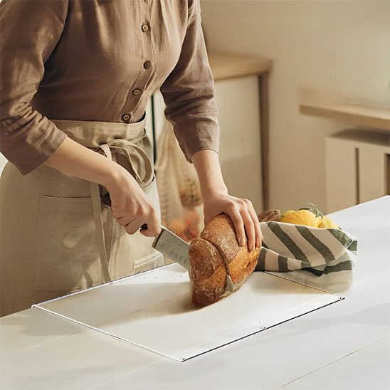 Femme coupe pain sur Planche à découper avec rebord sur comptoir blanc